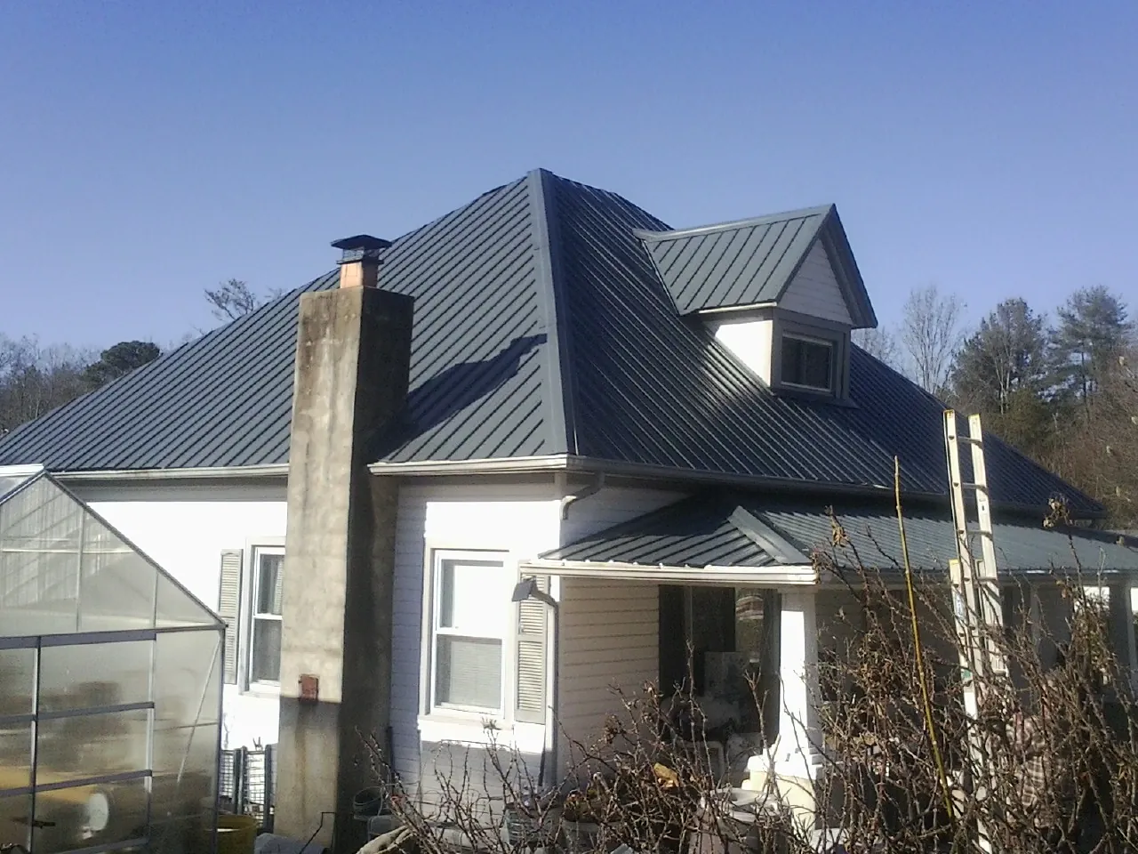Dark blue standing seam metal roof on a white farmhouse with dormer — Slate & Tile Roof Repair by Roofing Brothers in Starkville