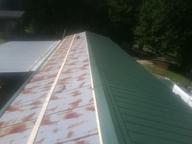 Old rusted panels beside newly installed green metal roofing — Wind Damage Roof Repair by Roofing Brothers in Starkville