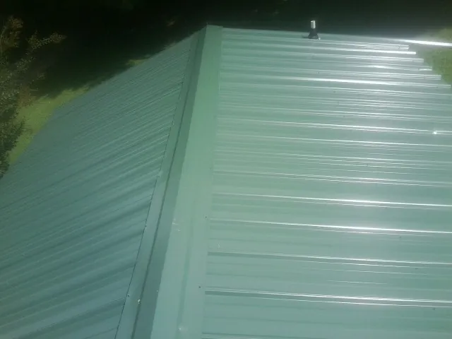 New green metal panels meeting at the ridge of a roof — Flat Roof Repair work by our crew in Starkville