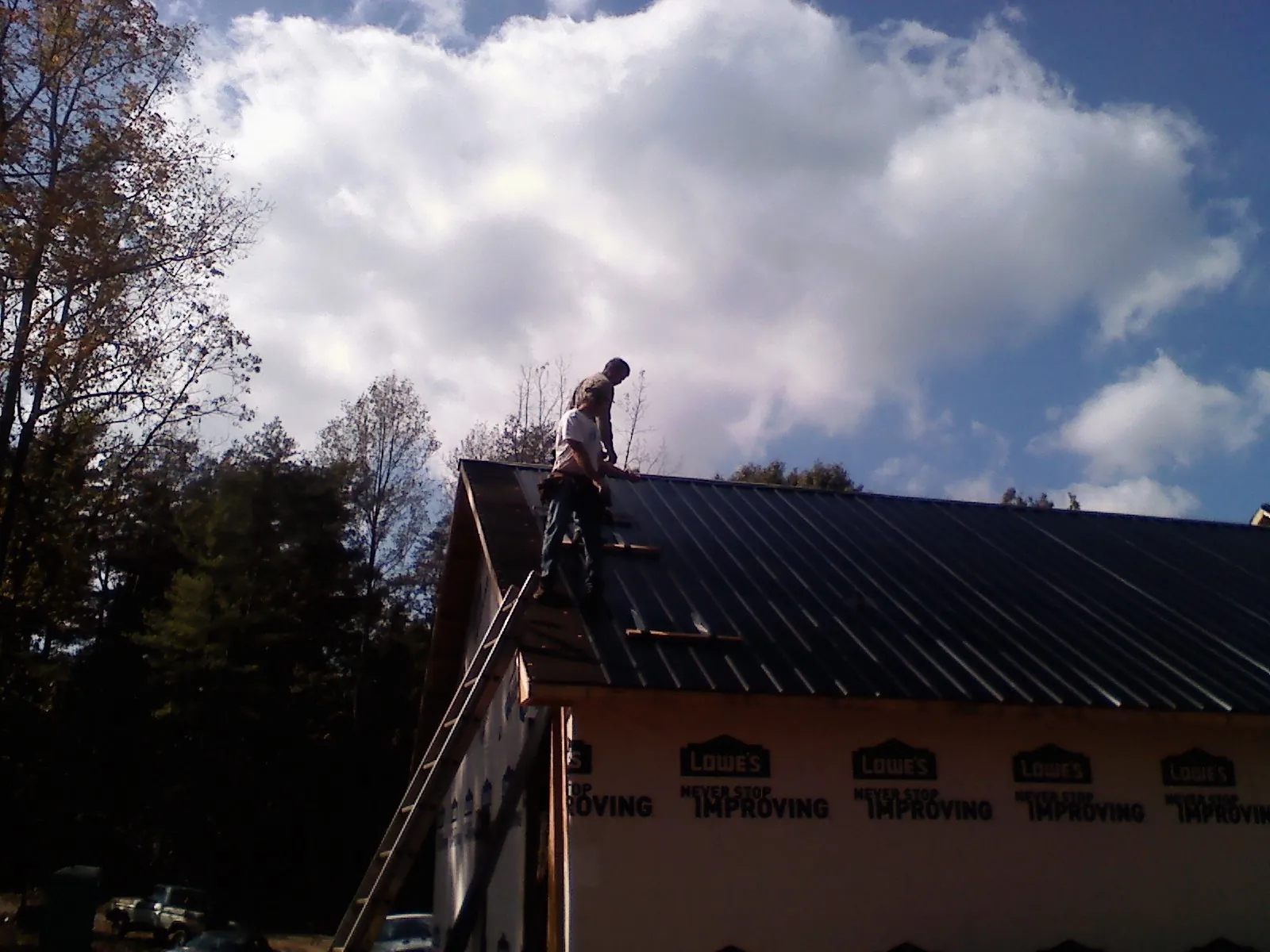 Roofer fastening dark metal panels high against a cloudy sky, from a Roof Inspection job in Starkville