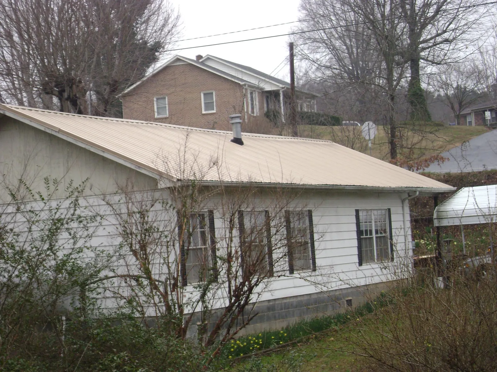 Tan metal roof on a white sided house set into a hillside — Commercial Roofing by Roofing Brothers in Starkville