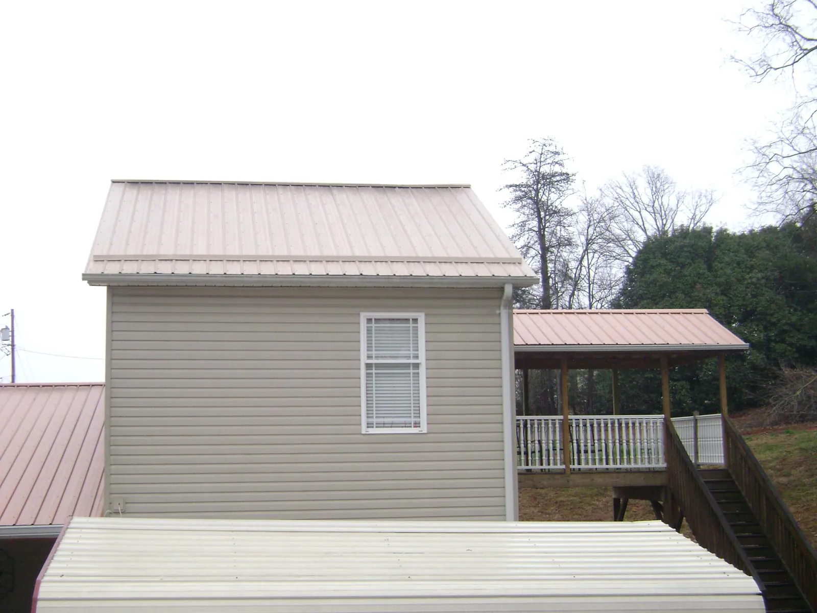 Tan metal roofs on a two story addition and attached porch, from a Roof Replacement job in Starkville